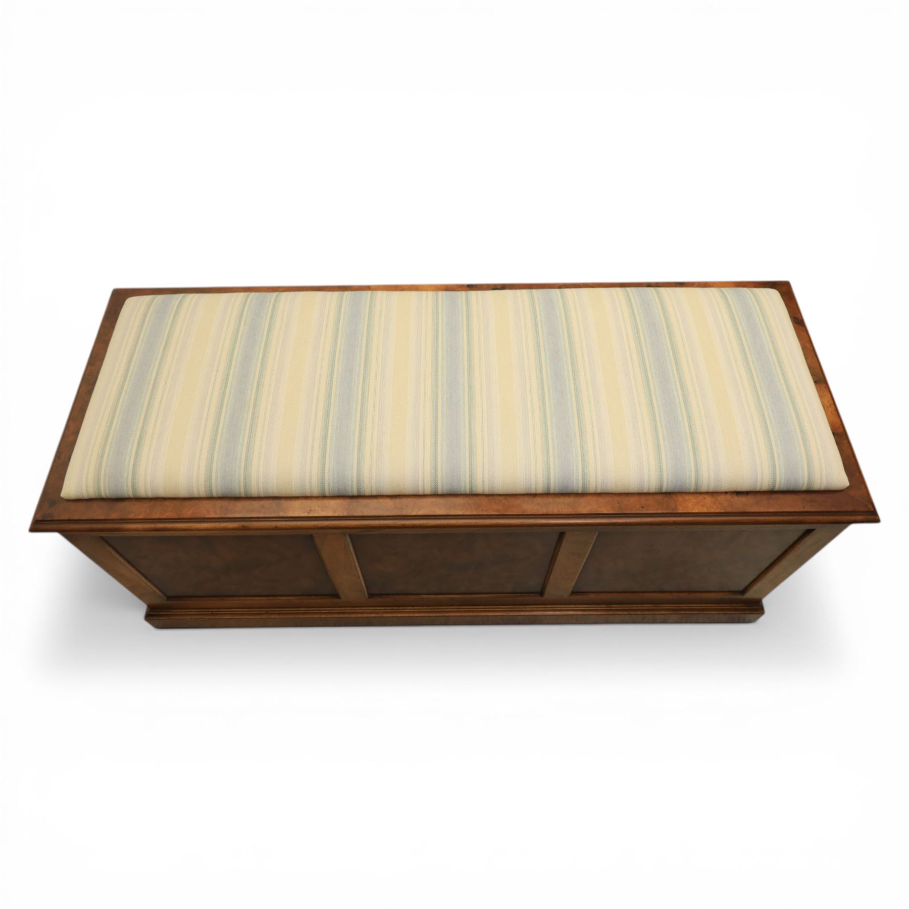 Traditional design figured elm blanket chest, with padded striped upholstered seat, over a hinged top with panelled sections below raised on a plinth base
