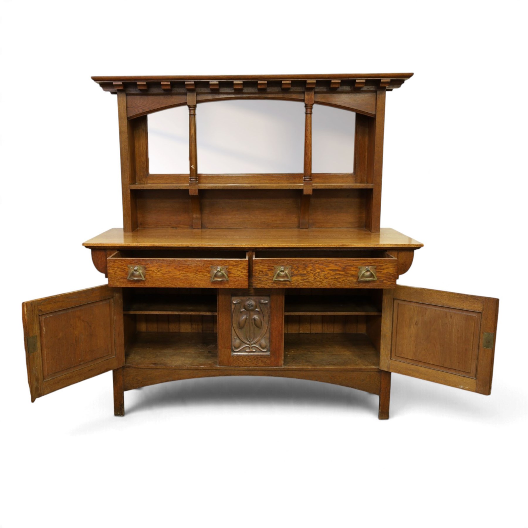 Art Nouveau oak mirrored sideboard, in the manner of Liberty's London, the raised back fitted with bevelled mirror plates divided by turned supports beneath a projecting cornice, above two drawers and panelled cupboard doors, the central panel applied with stylised floral carved panel, raised on shaped feet