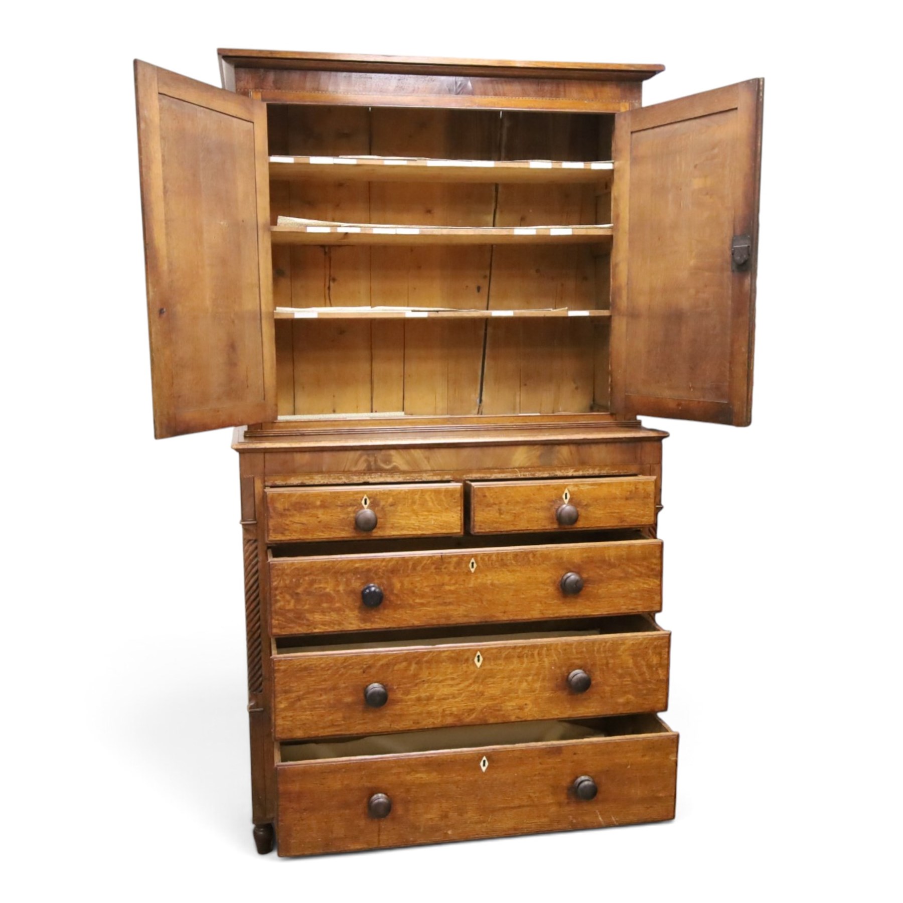 Georgian oak and mahogany housekeepers cupboard, the upper section with projecting cornice, crossbanded and inlaid frieze, above panelled doors with bone escutcheons, enclosing three fixed shelves, flanked by barley twist quarter pilasters, the lower section with further crossbanded and inlaid frieze, two short over two long graduating drawers with ebonised handles, raised on turned supports 