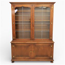 Late 20th century oak bookcase on cupboard, with moulded cornice above pair of astragal glazed doors with shaped inner frames enclosing adjustable shelves, the base with moulded top above two fielded panel cupboard doors with brass handles, upon compressed bun front feet 