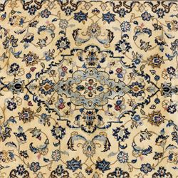 Central Persian Kashan hand-knotted carpet, ivory ground, with a central pale blue shaped floral medallion with pendants, surrounded by scrolling foliate and floral motifs incorporating rosettes, palmettes and delicate vine work in blue, cream and beige tones, enclosed by an ivory border with repeating palmettes and meandering vines, flanked by floral guard stripes, with cotton fringes