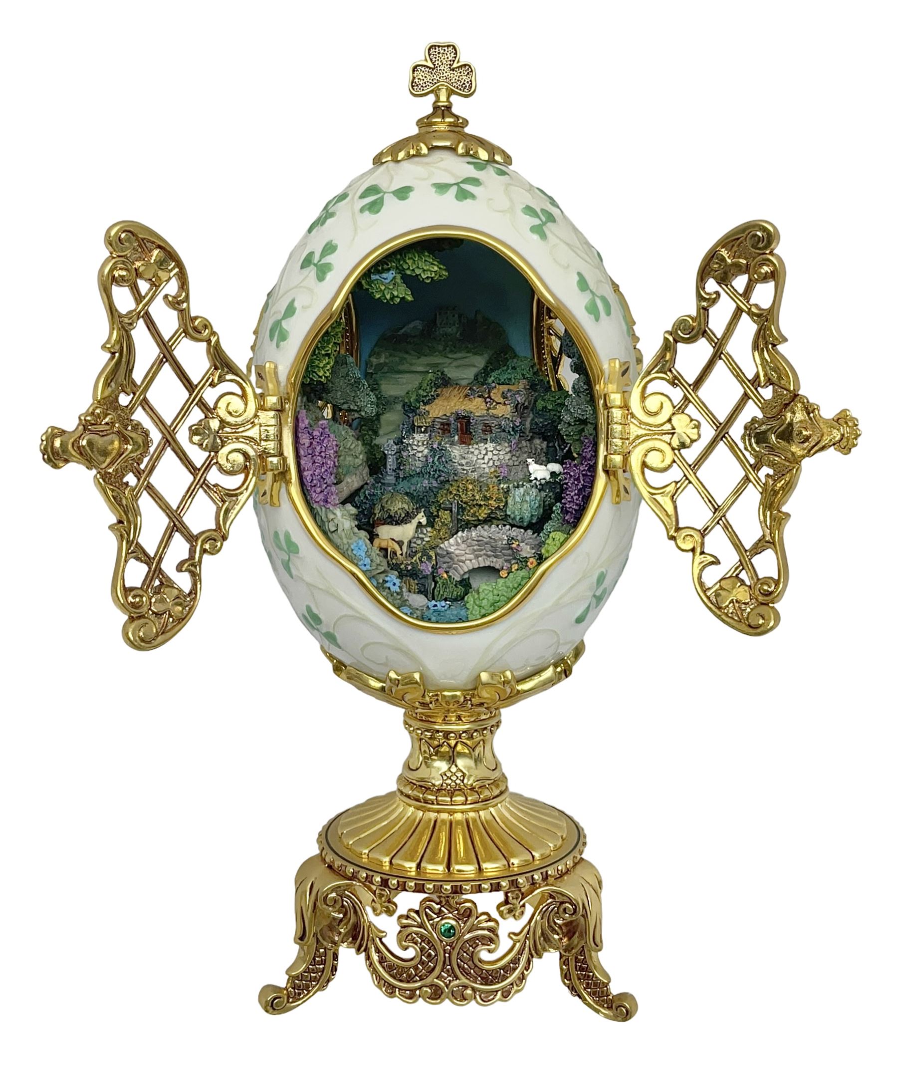 Franklin Mint The Emerald Isle Collector Egg, the egg decorated with embossed shamrocks upon a cream ground, with a gilded shamrock finial, accents and openwork door, opening to reveal a miniature landscape scene, upon three gilded feet set with green paste stones, with certificate of authenticity H23cm, 