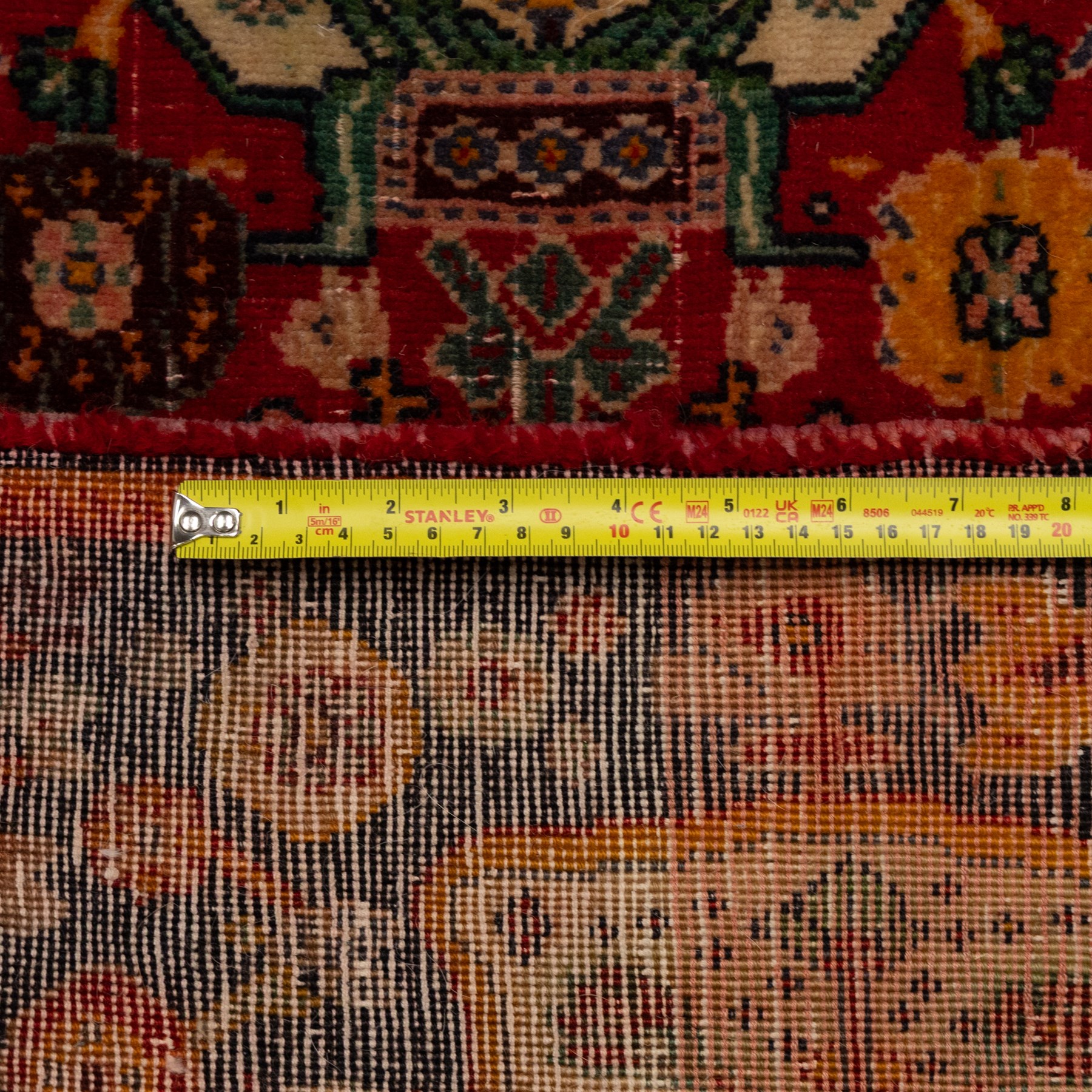 North Persian crimson ground rug, the field densely decorated with stylised flowering plants, urns and polychrome rosettes, within a stepped ochre outline, dark ground floral spandrels and geometric side panels