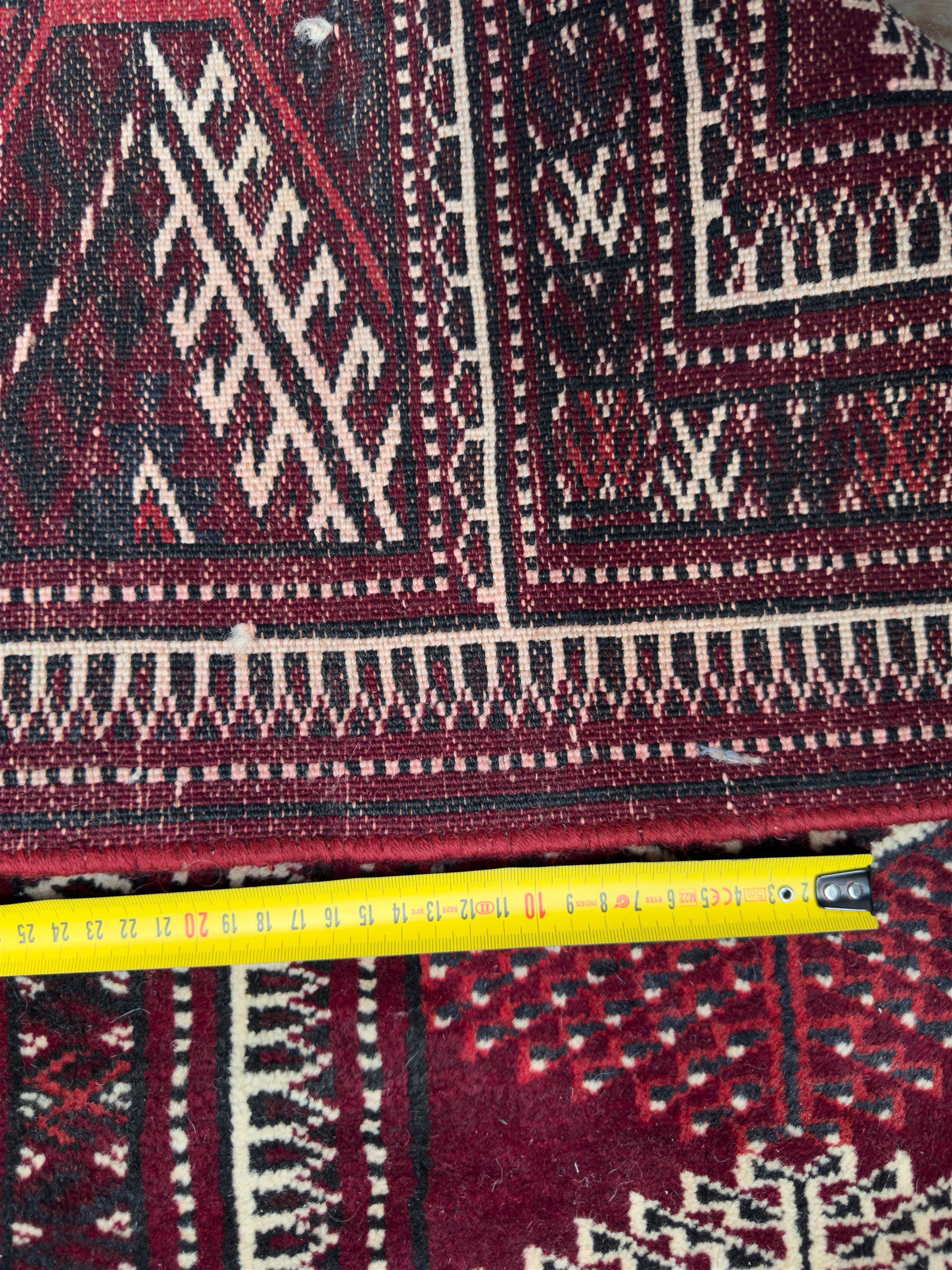 Northeastern Persian Yamut  hand-knotted carpet, the rich burgundy field with repeating rows of stepped gul motifs in cream and black, enclosed by multiple linear and geometric borders with hooked motifs and diamond medallions