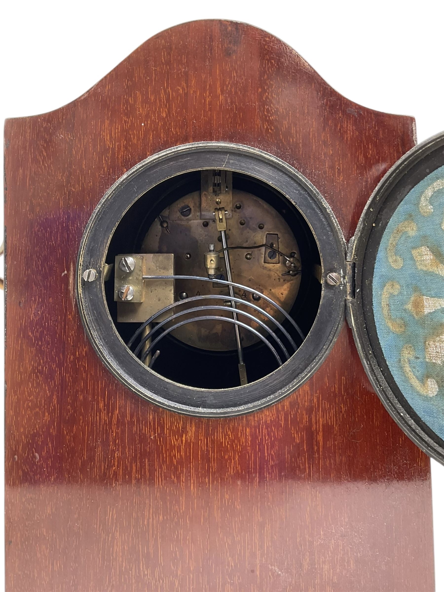 Edwardian- 8-day mantle clock in a mahogany case with a serpentine top and contrasting inlayed panels in satinwood and boxwood to the front, on a rectangular plinth raised on ball feet, silvered dial with Roman numerals and steel spade hands, twin train Parisian rack striking movement, sounding the hours and half hours on a coiled gong. With pendulum.
