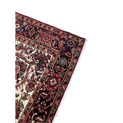 Persian Heriz red ground rug, central scrolled medallion on dark ground decorated with floral motifs, the surrounding field decorated with stylised plant motifs and smaller geometric symbols, guarded border with repeating pattern punctuated with rosettes and flower heads 