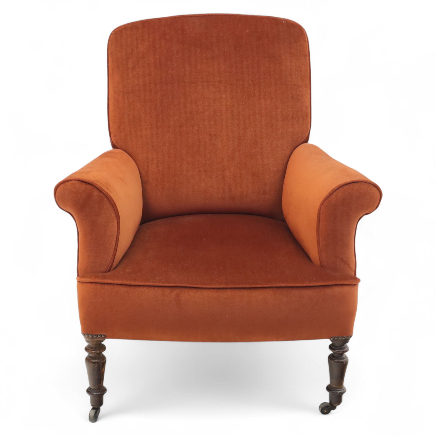 Late 19th century mahogany framed armchair, of generous proportion, upholstered in rust coloured velvet, with shaped back and scroll arms, raised on turned front legs with brass castors