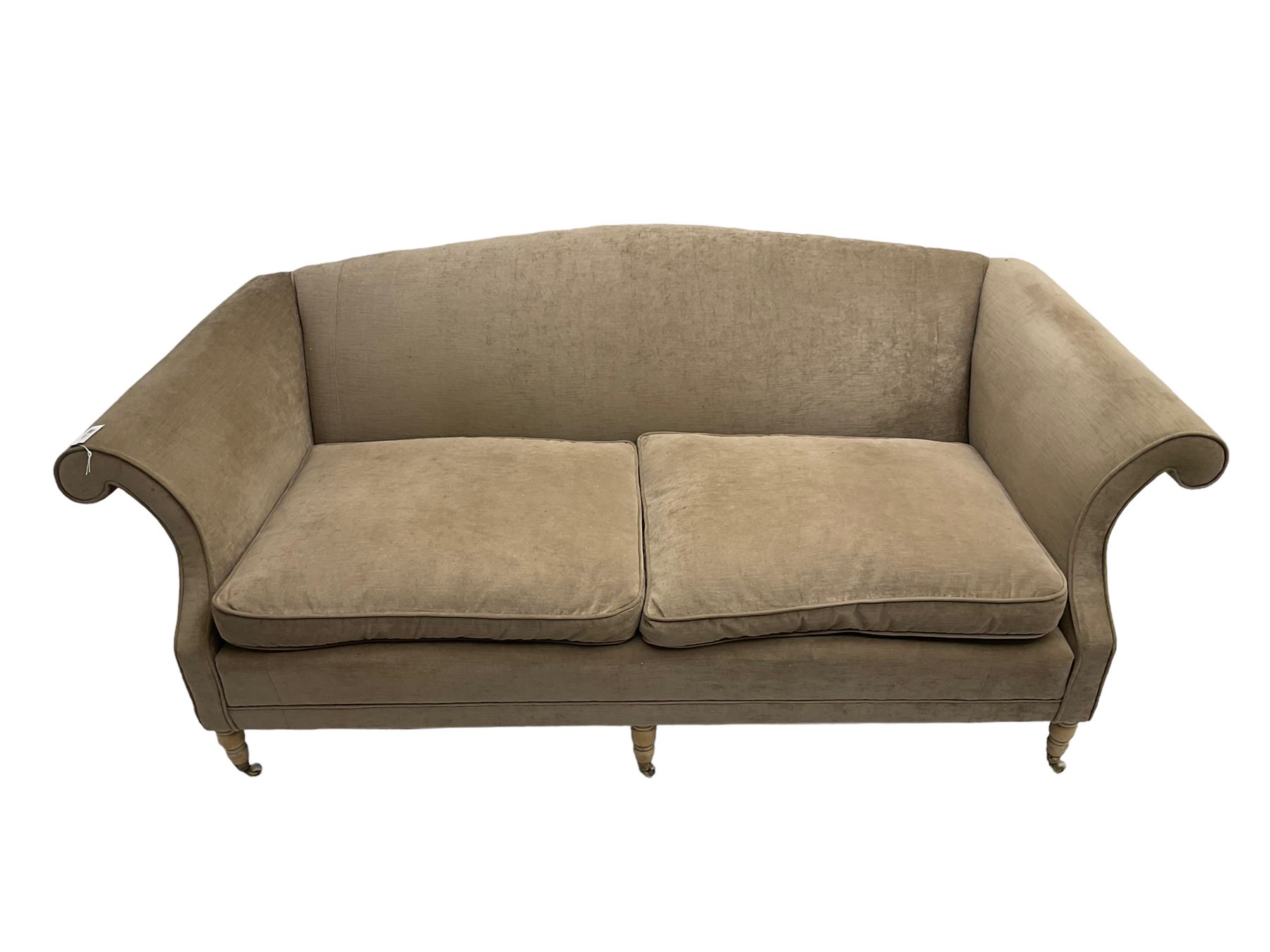 Traditional three seat sofa, curved back over scrolled arms, upholstered in crushed beige fabric with matching loose cushions, on turned front supports with brass and ceramic castors, together with matching footstool