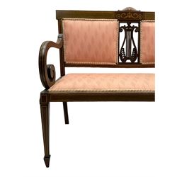 Edwardian inlaid mahogany two-seat settee or hall bench, the cresting rail inlaid with satinwood banding and boxwood stringing, central panel inlaid with scrolled leafy branches over pierced and carved lyre back, upholstered in peach fabric with repeating pattern, scrolled down sweeping arms, on square tapering supports with spade feet 