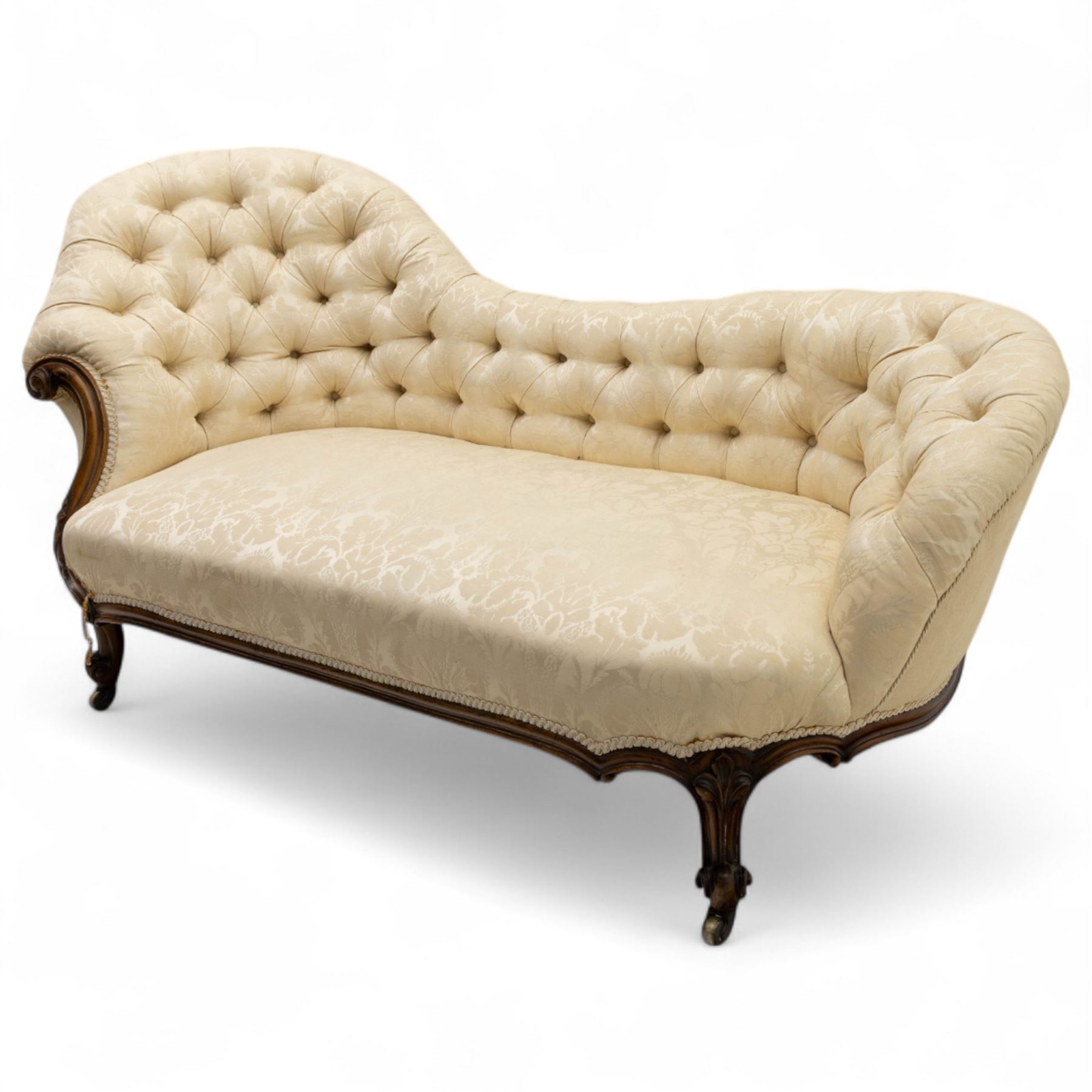 Late 19th century Victorian walnut button-back recamier, asymmetrical form, with cream damask fabric and gimp braid edging, shaped reeded apron above front and back scroll carved cabriole legs on brass castors