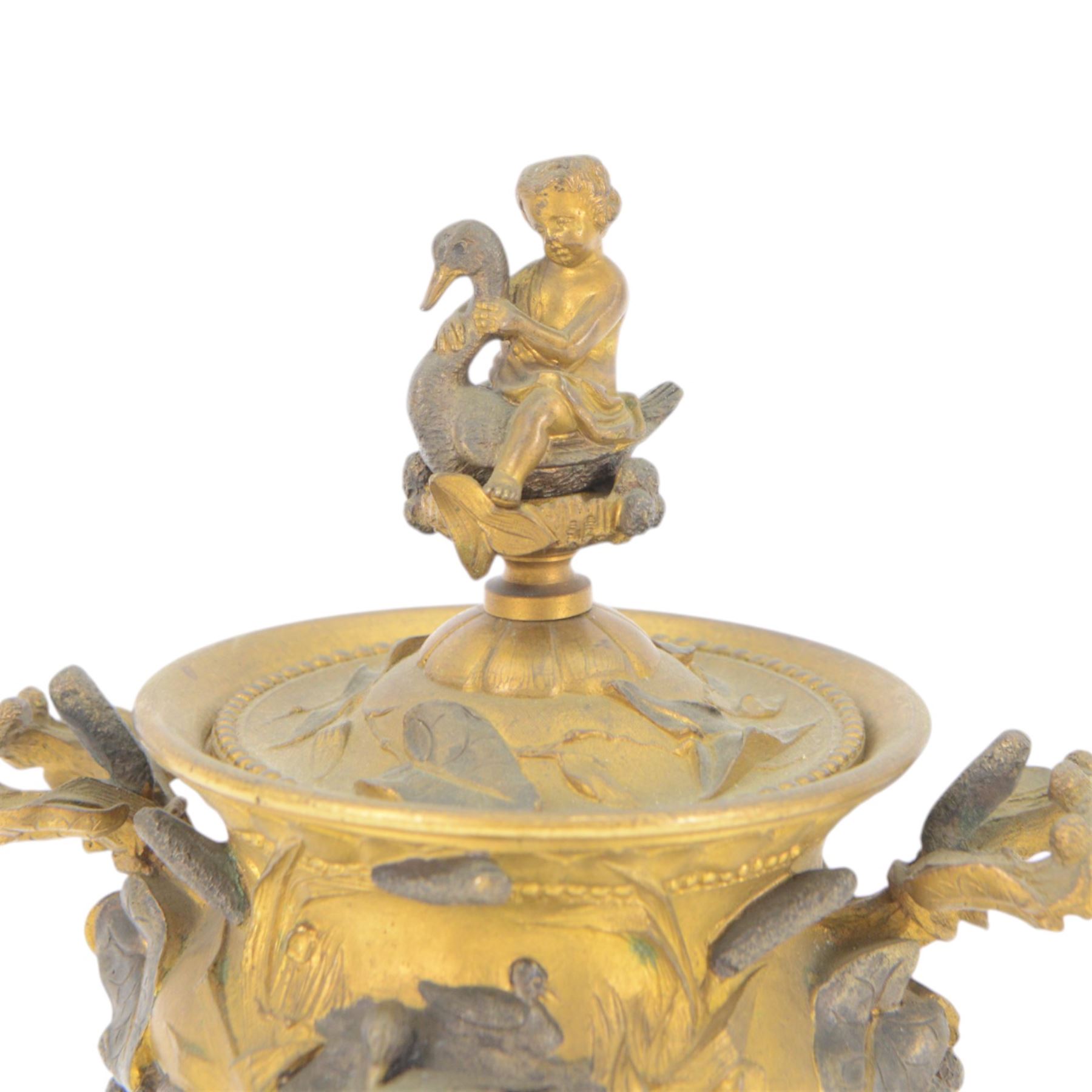 19th century gilt bronze twin handled urn, the removable cover with foliate decoration and finial modelled with a putti and swan, the body decorated in relief with swans and reeds, upon a circular foot, H19cm
