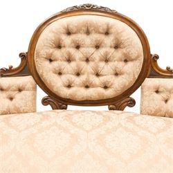 Victorian carved walnut framed double-ended settee with serpentine front, the central oval cameo back with flowerhead carved cresting rail, flanked by foliate C-scroll spandrels, the scroll carved arm terminals over floral carved cabriole supports with scroll feet and ceramic castors, the buttoned back and sprung seat upholstered in pale pink foliate patterned damask fabric
