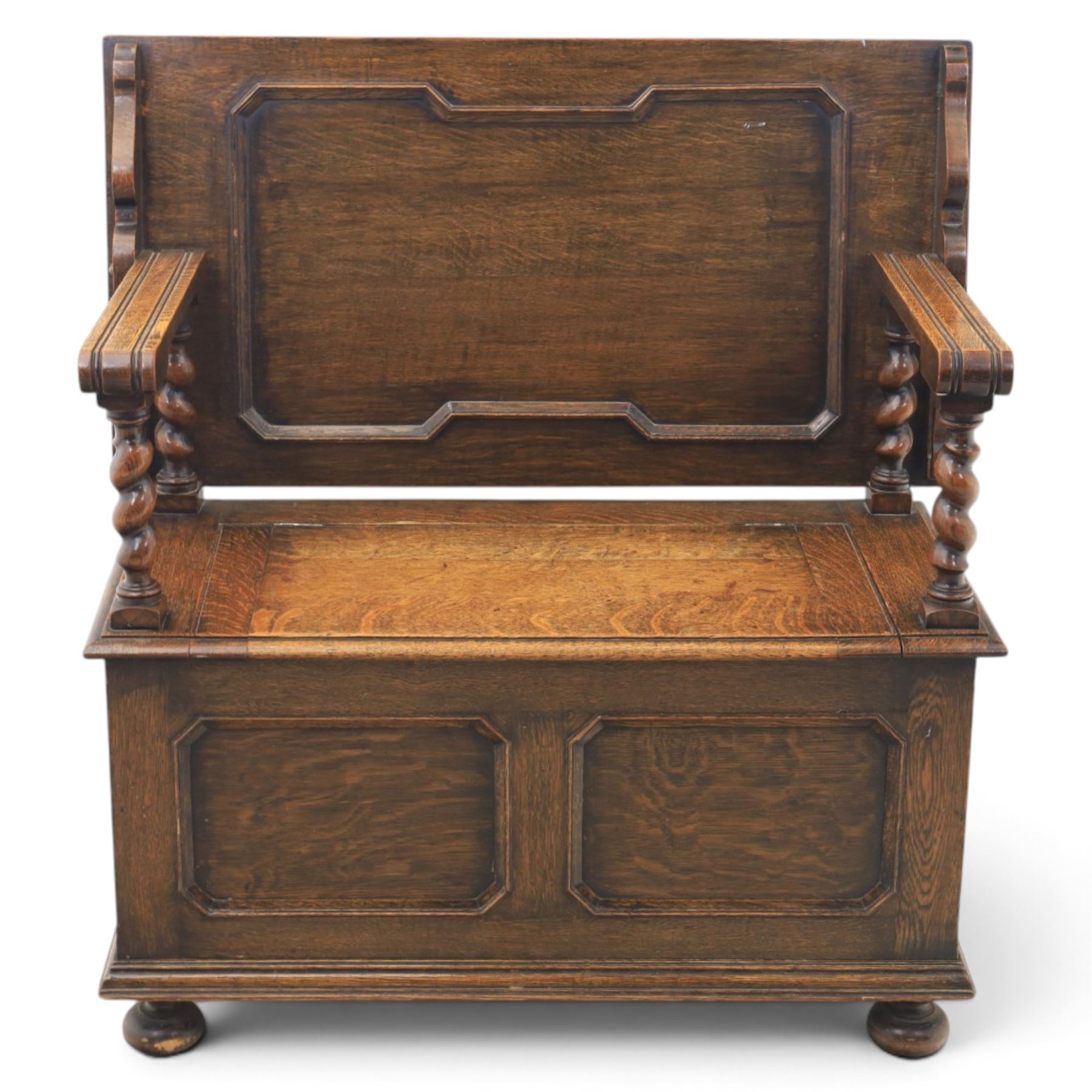 Early 20th century oak monks bench, panelled back converting to a table top, reeded armrests with barley twist uprights, hinged seat over panelled base supported on bun feet