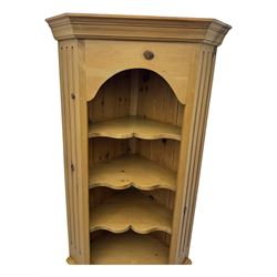 Early 20th century pine corner cabinet, projecting cornice over three shaped shelves, base fitted with single door enclosing storage space with a recessed panel, fluted sides, on plinth base