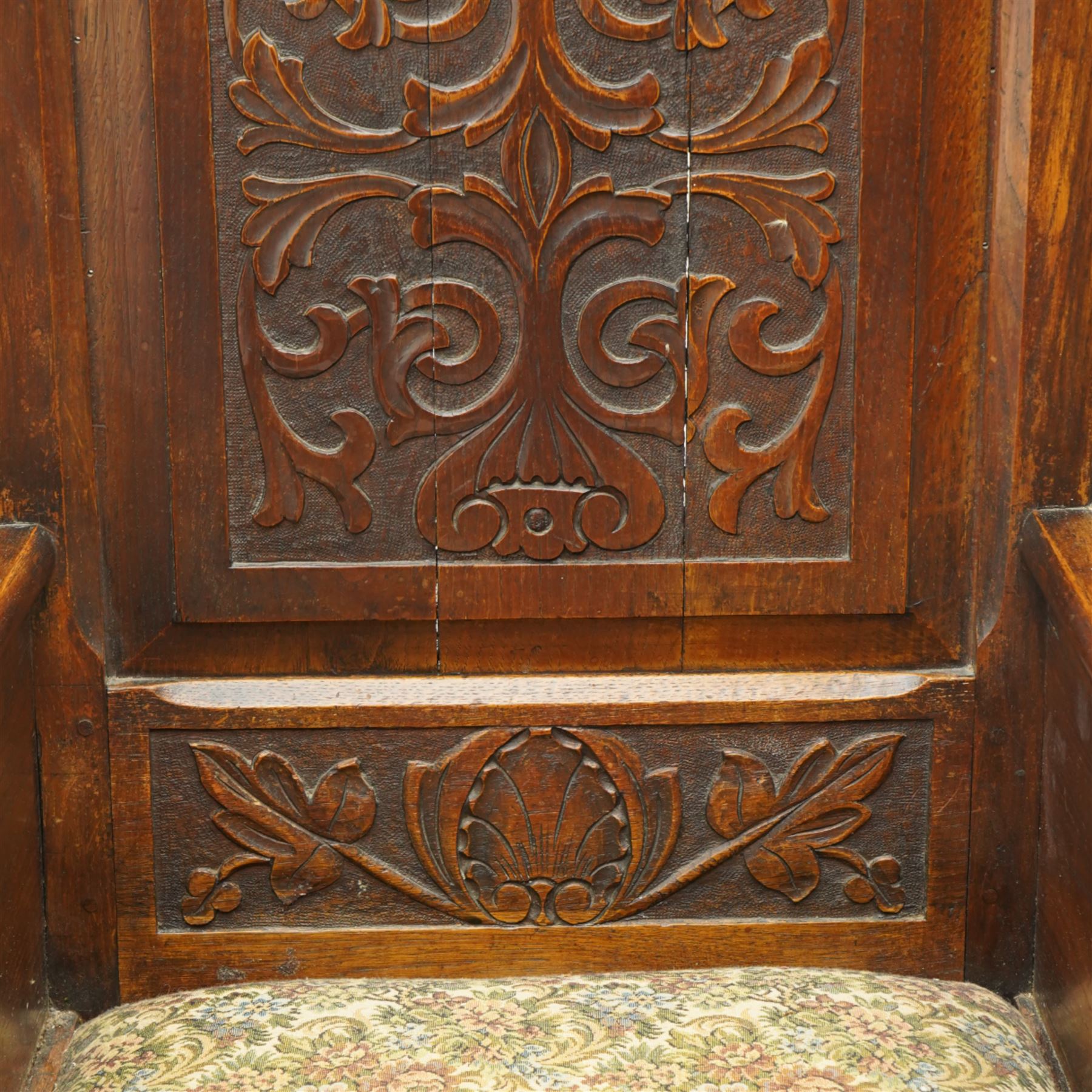 18th century design oak lambing chair, flower head and foliate carved cresting inscribed '1715' over panelled back carved with scrolling leafy branches, enclosed by shaped wingbacks over arms and panelled sides, the side panels carved with shells and scrolled leafage, upholstered seat over single drawer with matching carved decoration, on stile supports 