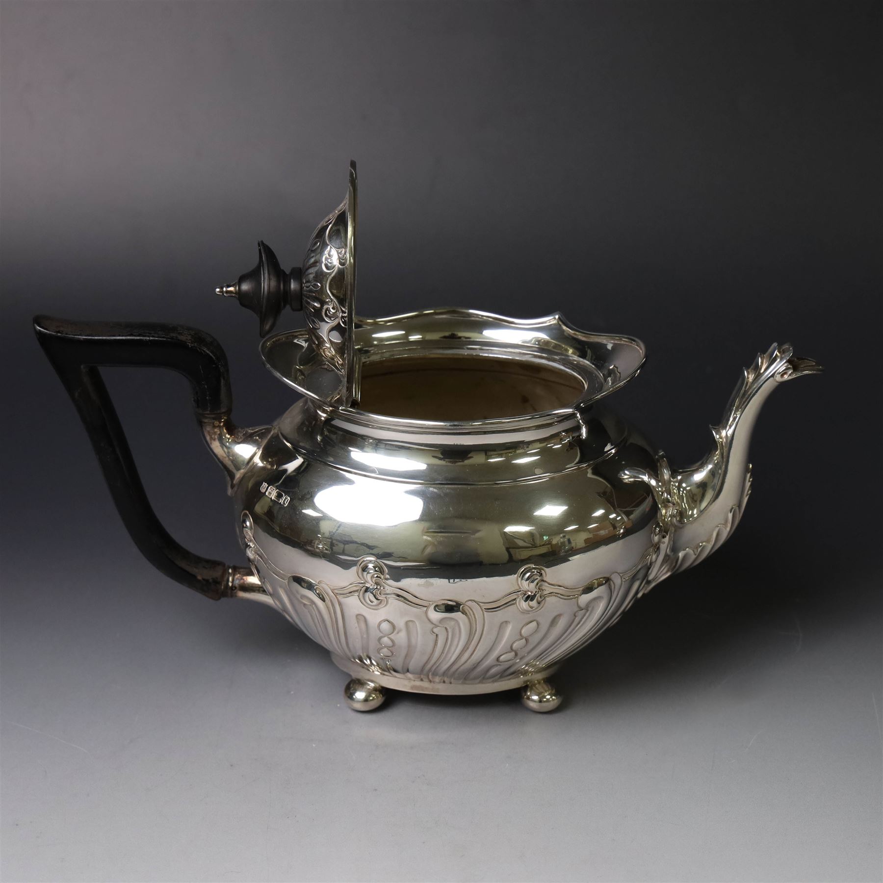 Edwardian silver three piece tea service, comprising teapot, twin handled open sucrier and a cream jug, each of oval form with embossed scrolling decoration and upon four bun feet, the teapot with ebonised wooden handle and finial, hallmarked Thomas Bradbury & Sons Ltd, Sheffield 1903, teapot H16cm