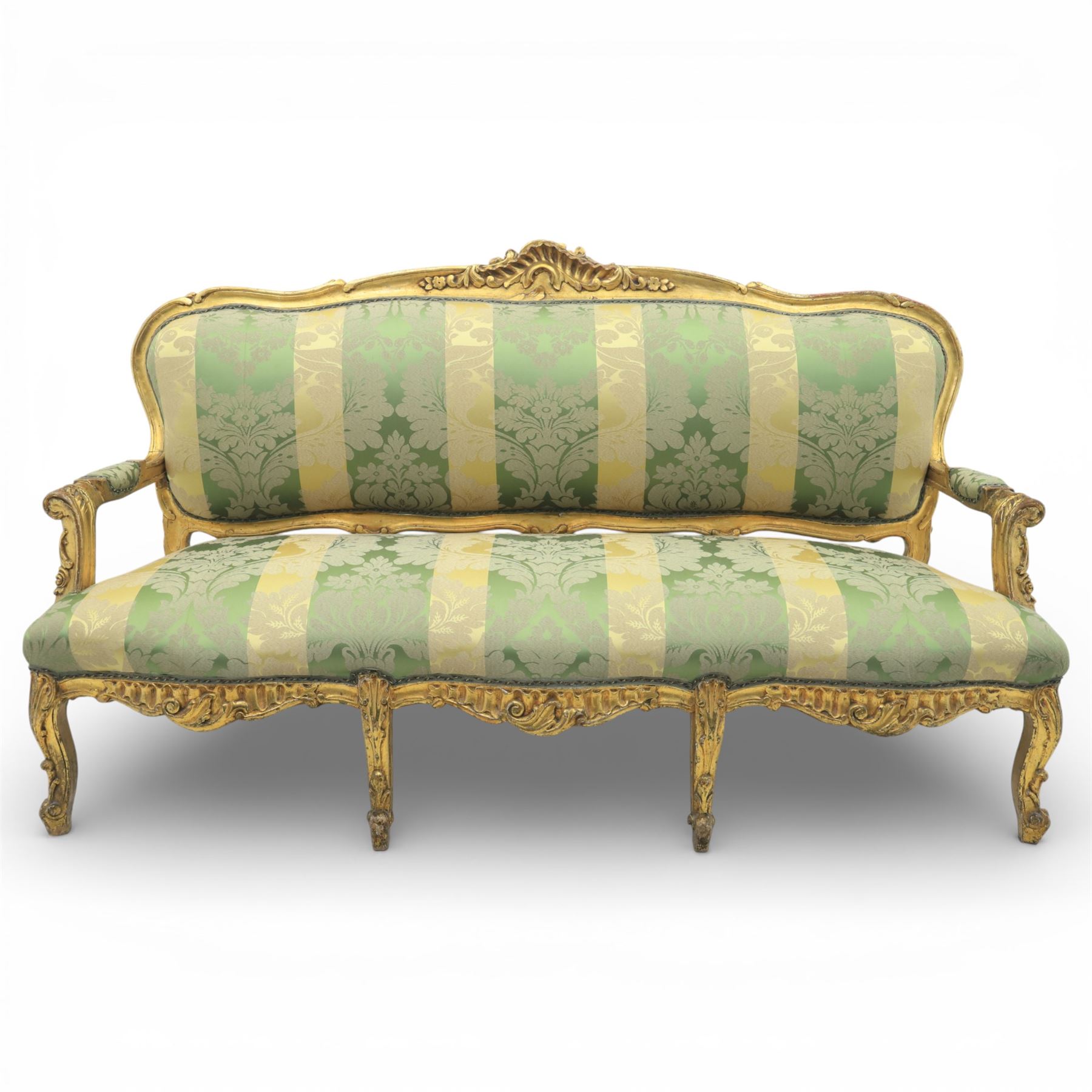 20th century French Louis XV style giltwood salon sofa, with shaped and moulded serpentine cresting rail carved with central scroll motif, padded back and seat upholstered in green and gold striped damask fabric, scroll carved open arms with padded rests, shaped apron carved with rocaille and foliate motifs, raised upon cabriole legs