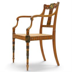 Late 19th century Adam Revival painted and parcel-ebonised satinwood open armchair, the cresting rail centred by a painted panel depicting putti holding garlands, within draped swag ornament and moulded ribbon-twists, over a pierced vertical splat with gilt beaded detail, the downswept arms and caned seat above a painted lattice and floral frieze, raised on ring-turned tapering front supports with musical instrument painted panel and acanthus leaves