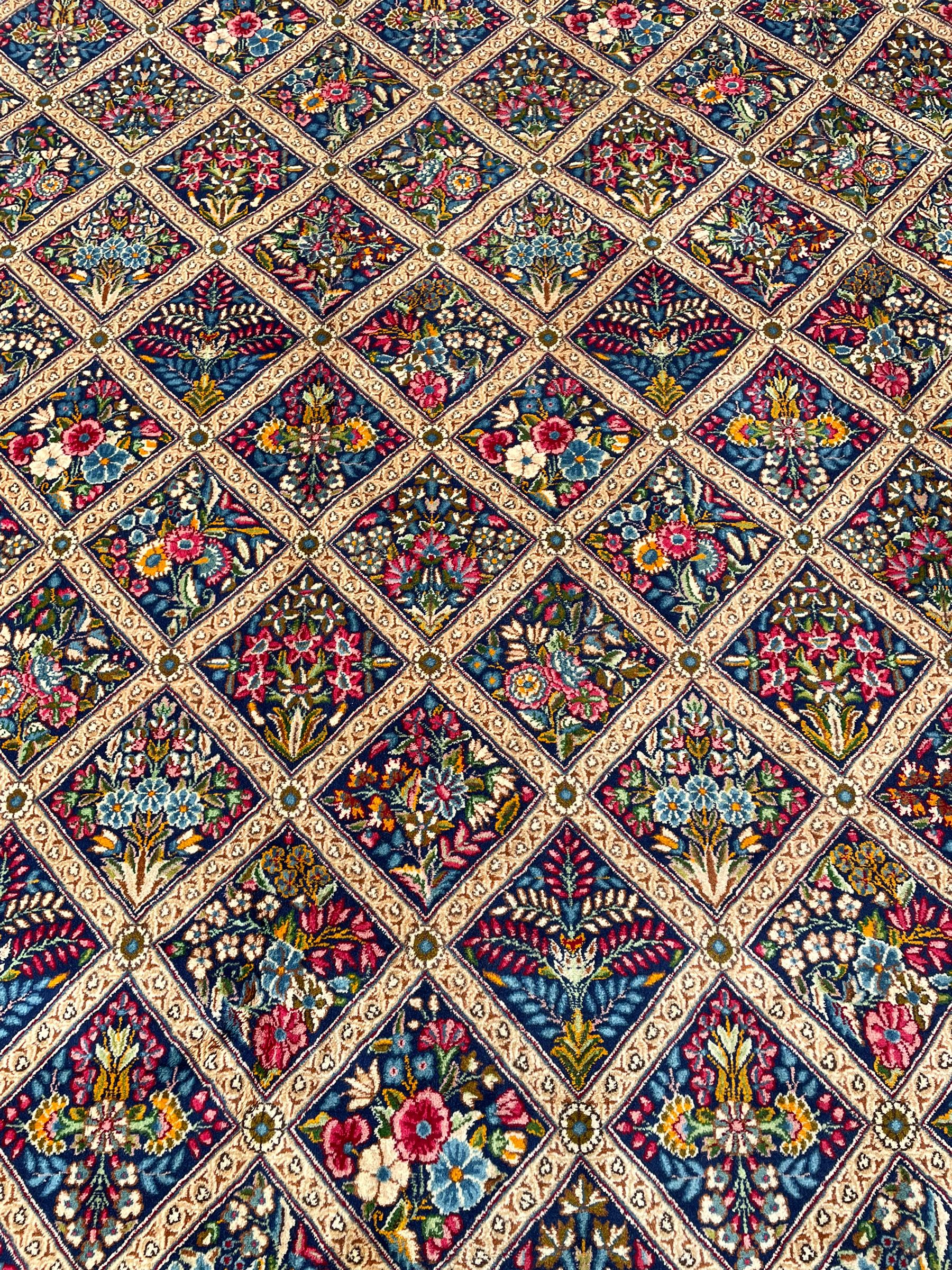 Persian Kirman indigo ground carpet, the field with repeating lozenge tiles with overall floral decoration, the main border with floral panels enclosed by the guards