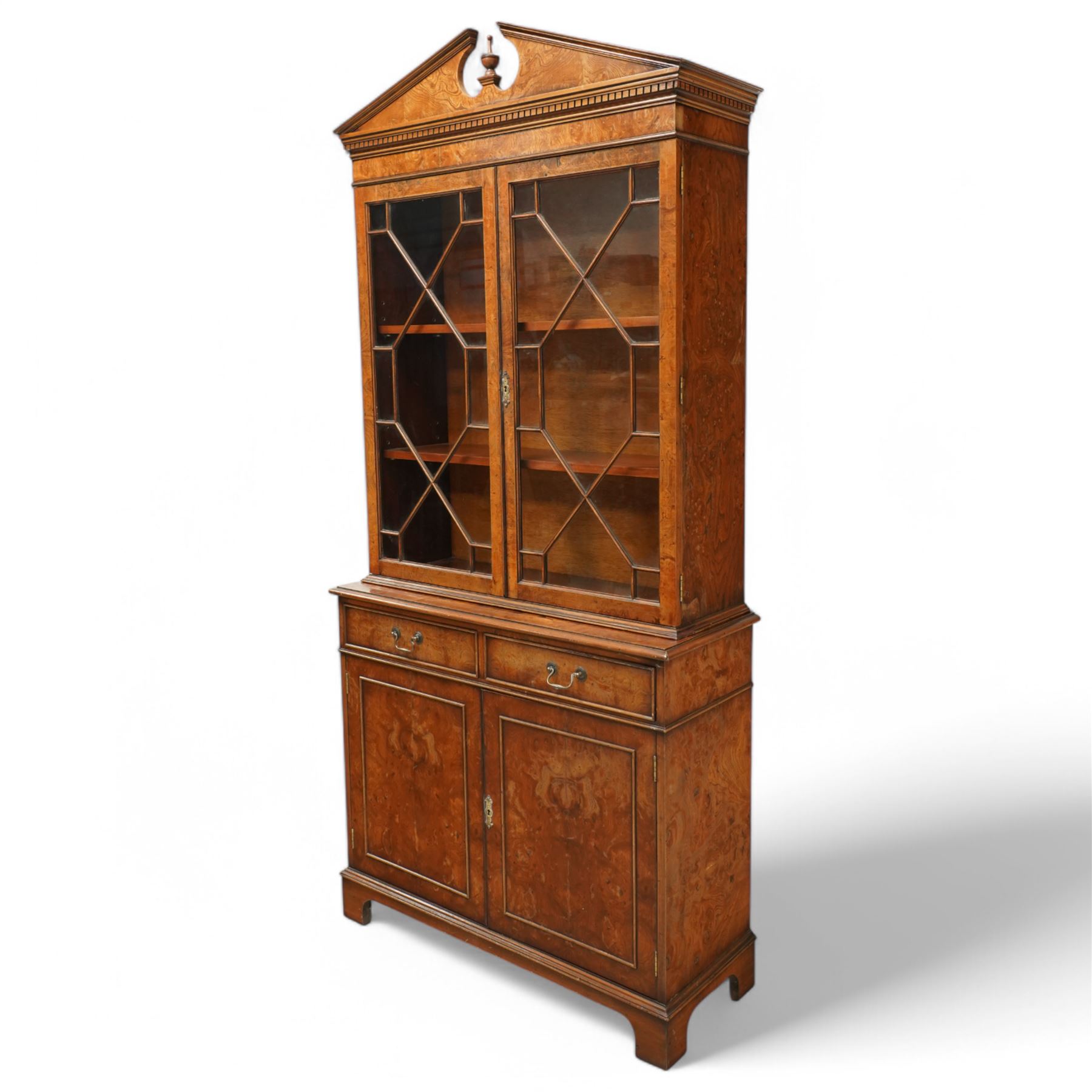 Georgian design Pollard -Oak bookcase cabinet over cupboard with panelled cupboards and two drawers, arched pediment above a dentil frieze and a pair of glazed doors enclosing adjustable shelves, raised on shaped bracket feet