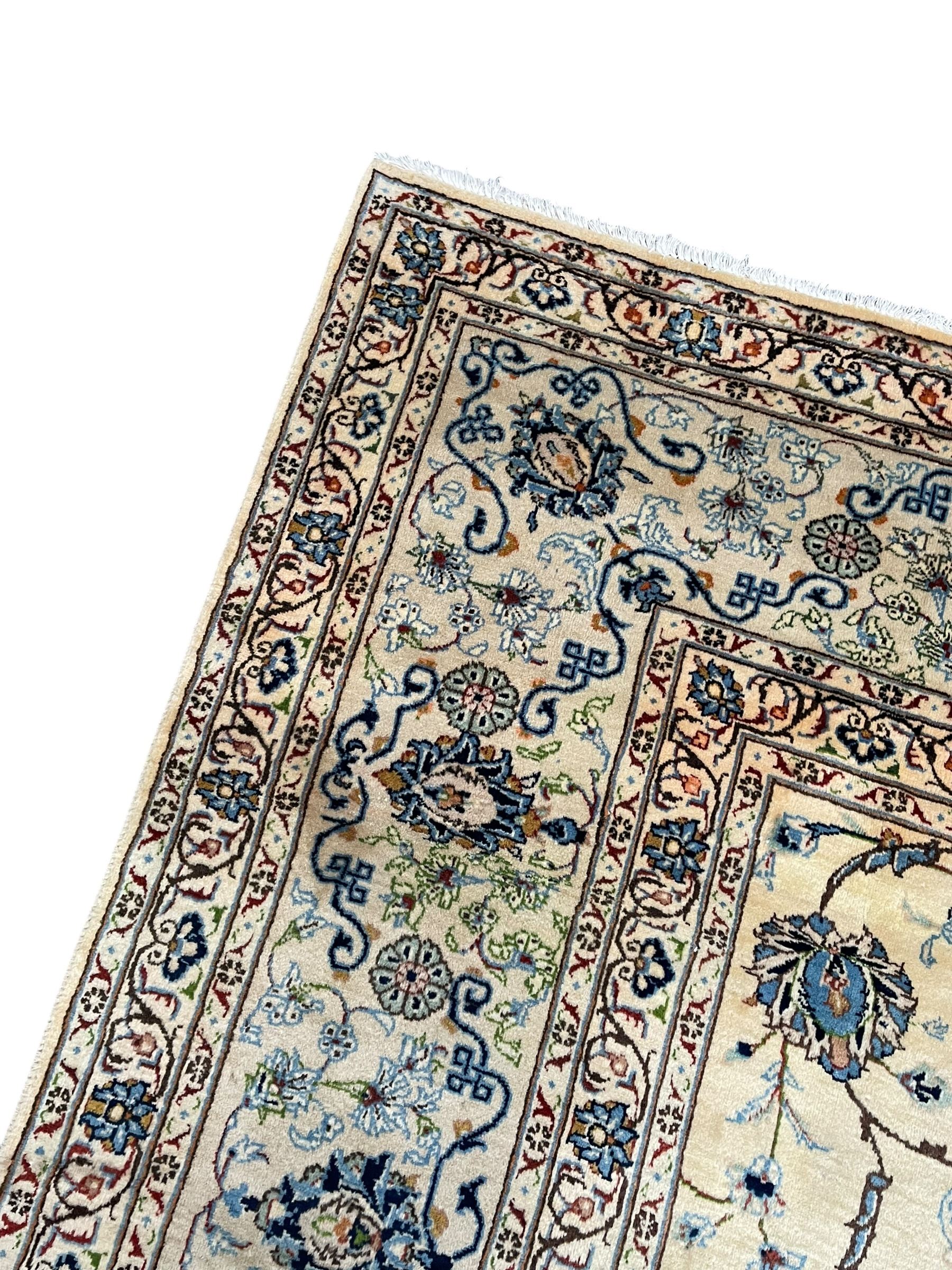 Persian Kashan ivory ground carpet, the field decorated with swirling foliate patterns and stylised plant motifs, scrolling border decorated with palmettes, within floral pattern guard stripes 