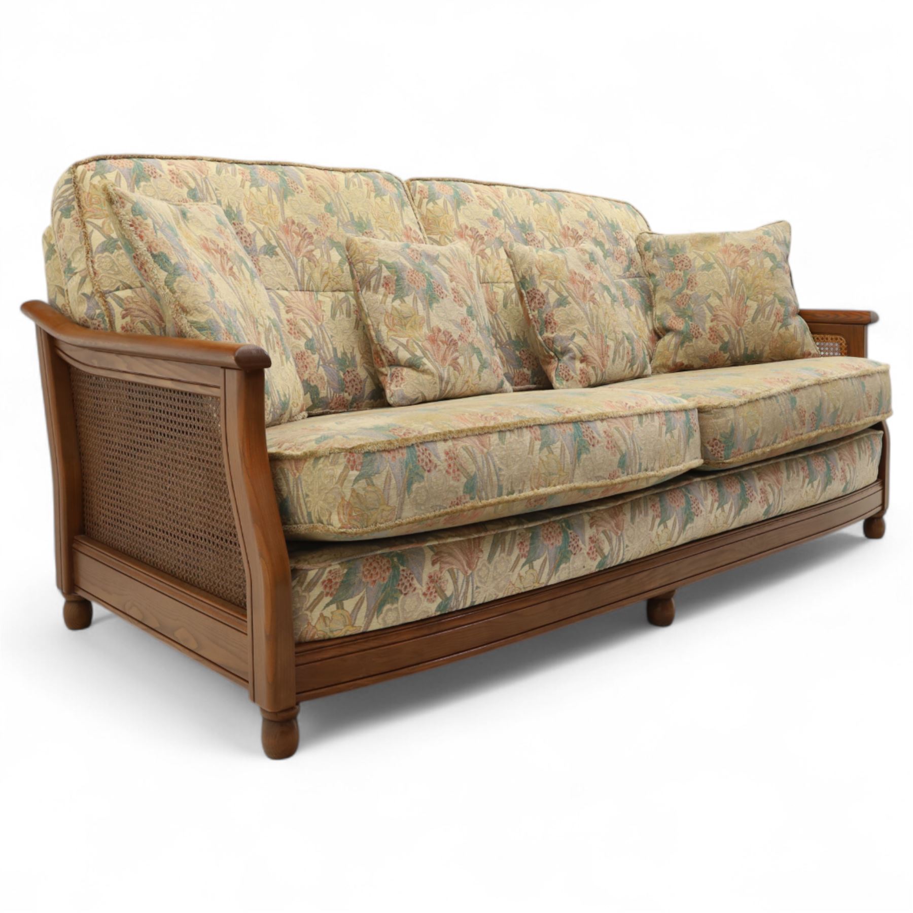 Ercol – bergère four piece suite, including armchair, two seat sofa, three seat sofa and footstool, all with removable floral upholstered cushions, the frames with side caning and rounded arm supports in stained beech

Three seat (H 87cm, D 89cm, W 196cm)
Two seat (H 87cm, D 89cm, W 137cm)
Armchair (H 87cm, D 89cm, W 87cm)
Footstool (H 28cm, D 55cm, W 55cm)