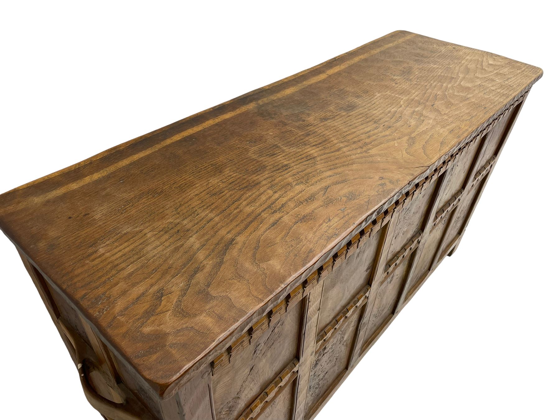 Gnomeman - oak blanket box, all-over adzing, the hinged top over figured and burr panelled front, decorated with carved crenellations and arcade, carved with gnome signature, pierced handles to each end forming the central rail, wrought metal hinges, on stile supports, by Tom Whittaker, Littlebeck, Whitby