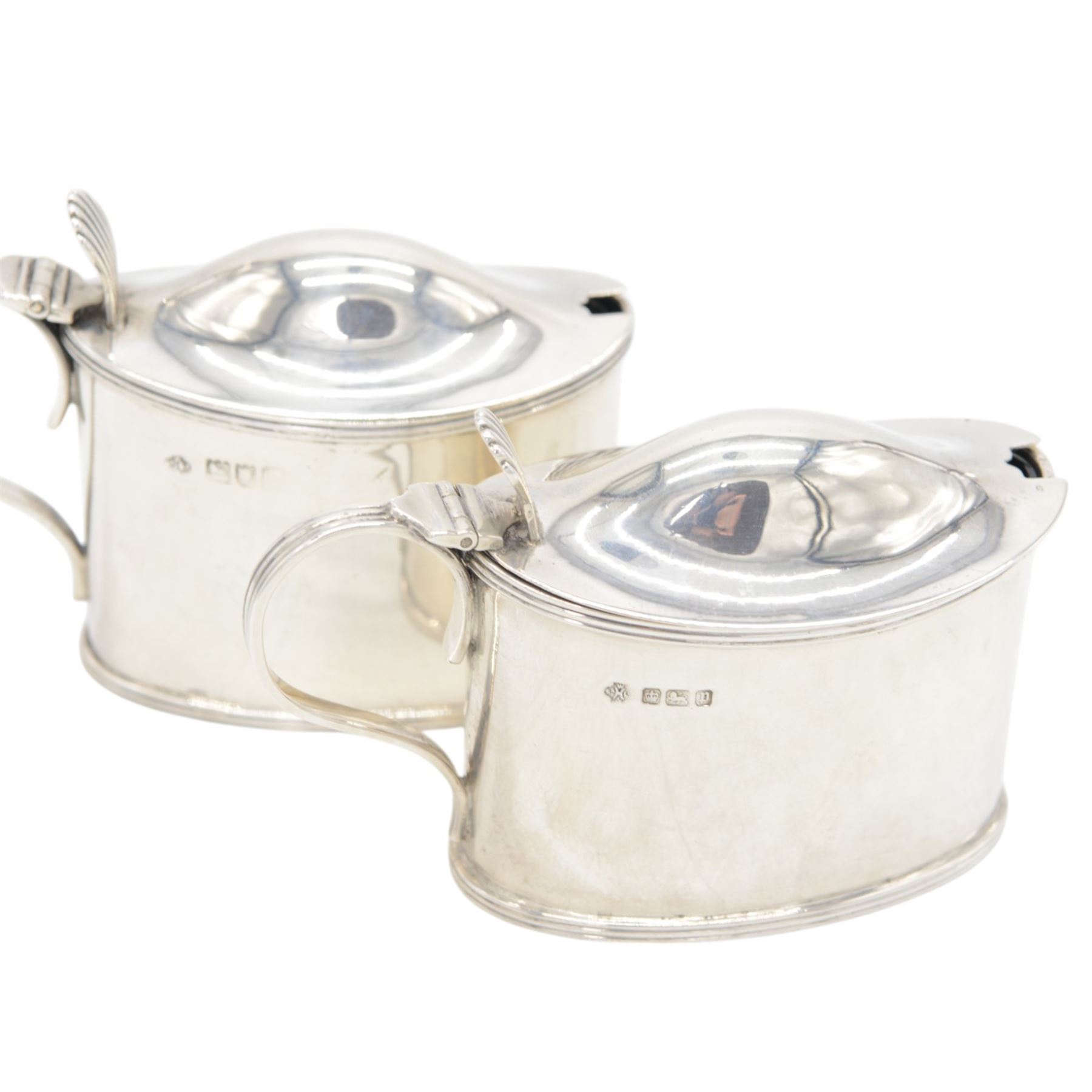 Pair of Edwardian silver mustard pots, of oval form with reed borders and palmette thumb pieces to hinged covers, opening to reveal blue glass liners, hallmarked William Hutton & Sons Ltd, London 1905, H7.5cm