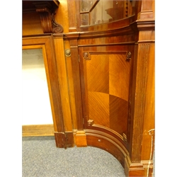  Large Edwardian Adam style mahogany chimney-piece, fire-surround with swan neck pediment and urn finial above circular bevelled mirror plate with two candle branches, enclosed by concave corner cupboards with moulded cornice, blind fret frieze and astragal glazed doors above a quarter veneered panel doors on a skirted base, H340cm, W269cm, D70cm, aperture 107cm x 102cm  