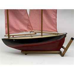 Mid-20th century pond yacht with red and black painted wooden hull, simulated planked deck bearing plaque for 'Hamleys 200-202 Regent Street London W1', two masts and sails and working rudder W65cm H89cm, on slatted pine stand