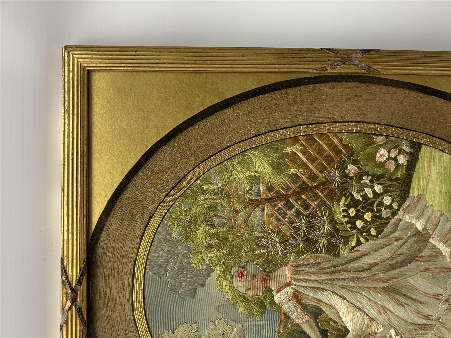 George III silkwork picture, of oval form depicting a female figure in garden setting, within a silkwork border detailed with verse from Robert Burns Bonnie Peg, 'Her air sae sweet, and shape complete, The Queen of Love did never move, Wi' Motion mair enchanting!', and monograms 'FV' and 'SM', in reeded gilt frame and gilt mount, indistinctly inscribed in pencil verso, overall H36cm L30.5cm