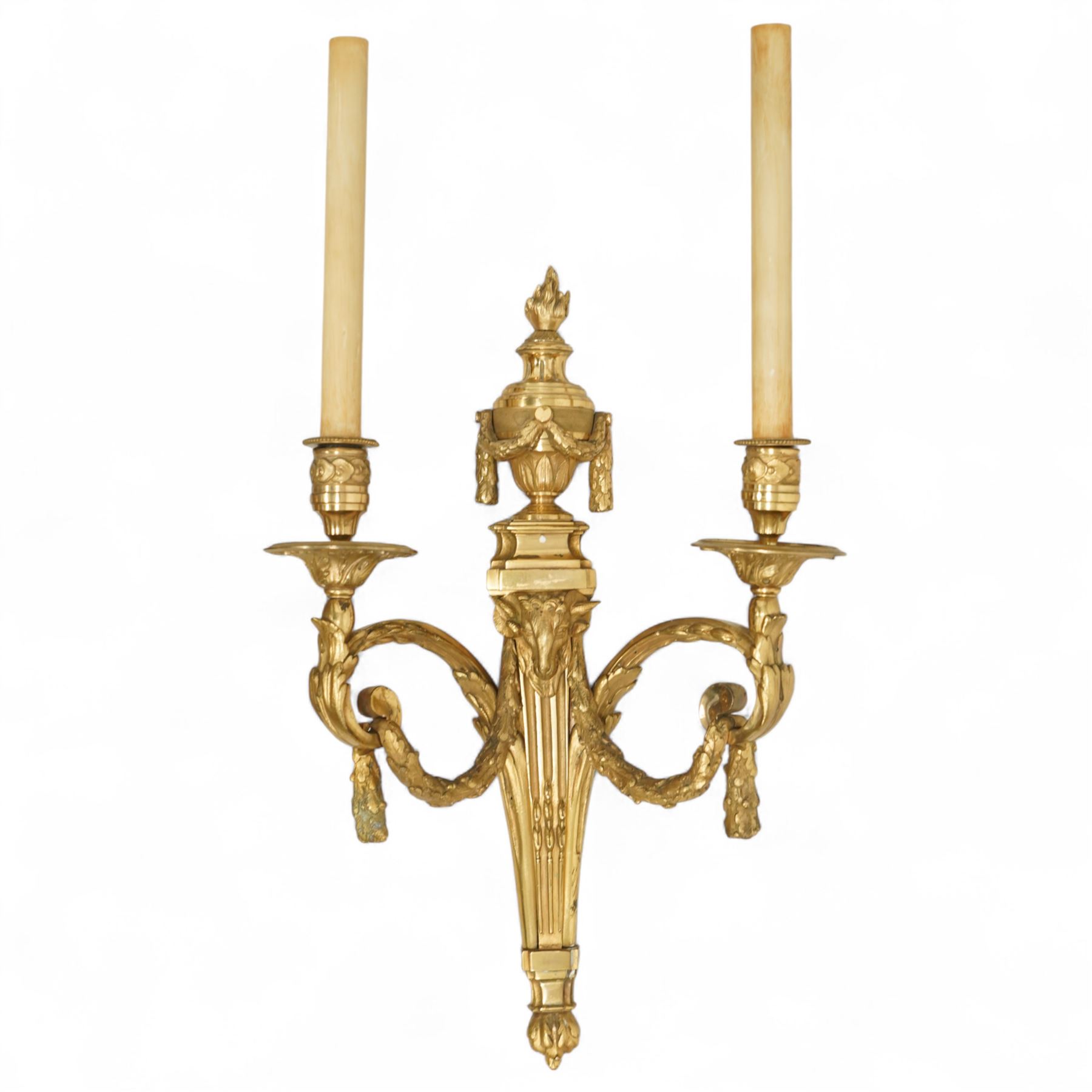 Pair of 19th-century Louis XVI-style ormolu rams-headed two-light wall appliques, the arms joined by a garland of laurel leaves, the half fluted stem surmounted by a vase with laurel garland, wired for electricity 
