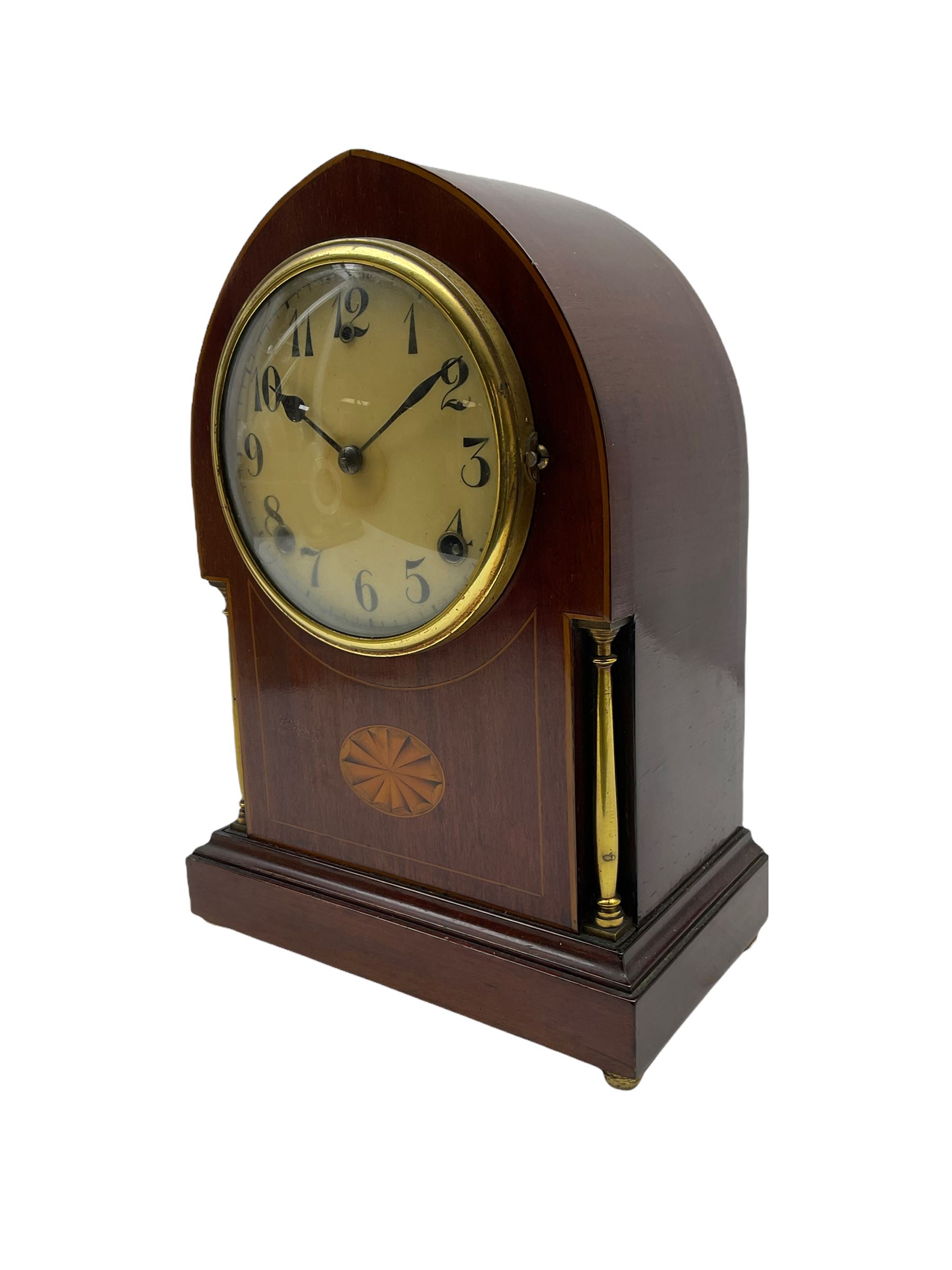 A late 19th century American  mantle clock in a “Lancet” case manufactured by the  Gilbert Clock Factory, Connecticut,  mahogany veneered case with an oval inlay, satinwood stringing to the edge and two recessed brass pillars, on a moulded plinth with four bun feet, enamel dial with upright Arabic numerals and spade hands, fast/slow regulation, with a convex glass and spun brass bezel, eight-day movement striking the hours and half hours on a coiled gong. No pendulum.