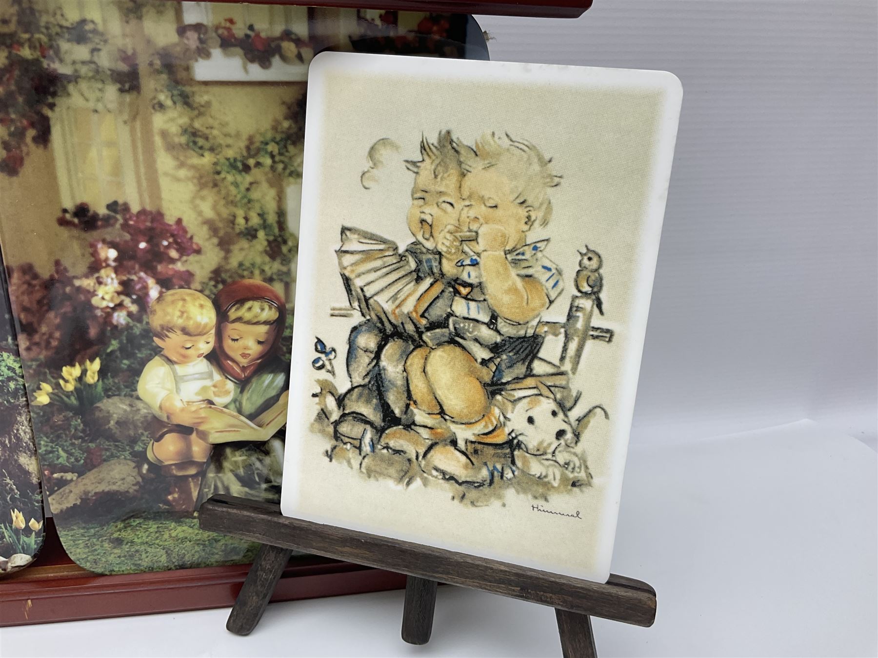 Two ceramic Hummel postcards by Goebel, both displayed on wooden easels, together nine Hummel eggs, set of four Hummel School Days plates, on wooden hanging rack, Goebel Collectors Club Member plaque etc