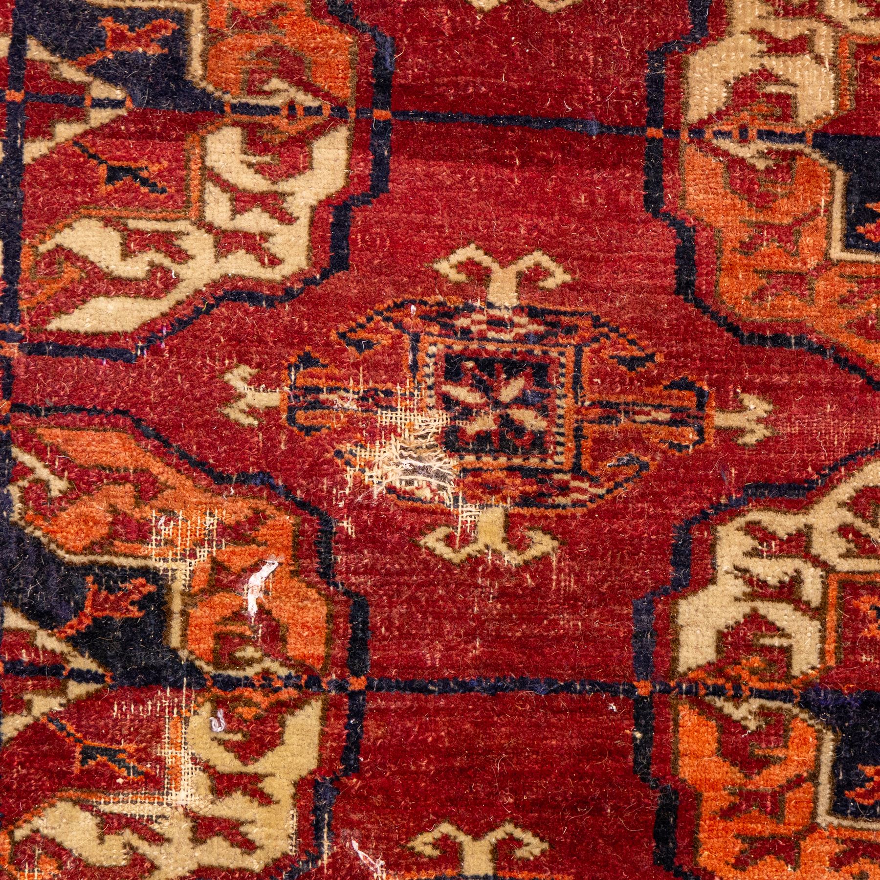 Vintage Bokhara hand-knotted rug, madder field woven in rows of octagonal Tekke guls arranged in vertical columns, each enclosing angular cruciform devices and tribal motifs, divided by narrow indigo lines, within multiple geometric borders incorporating stepped lozenges and latch hook devices, with cotton fringe ends 