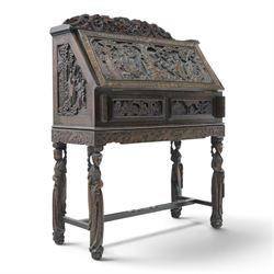 Early 20th century Chinese export carved hardwood writing bureau, the sloped fall front deeply carved with a narrative figural scene beneath pine and prunus trees, above a pair of rectangular carved panels, the shaped crest rail with entwined dragons, interior fitted with pigeonholes and a central drawer, on figural front supports with shaped stretcher