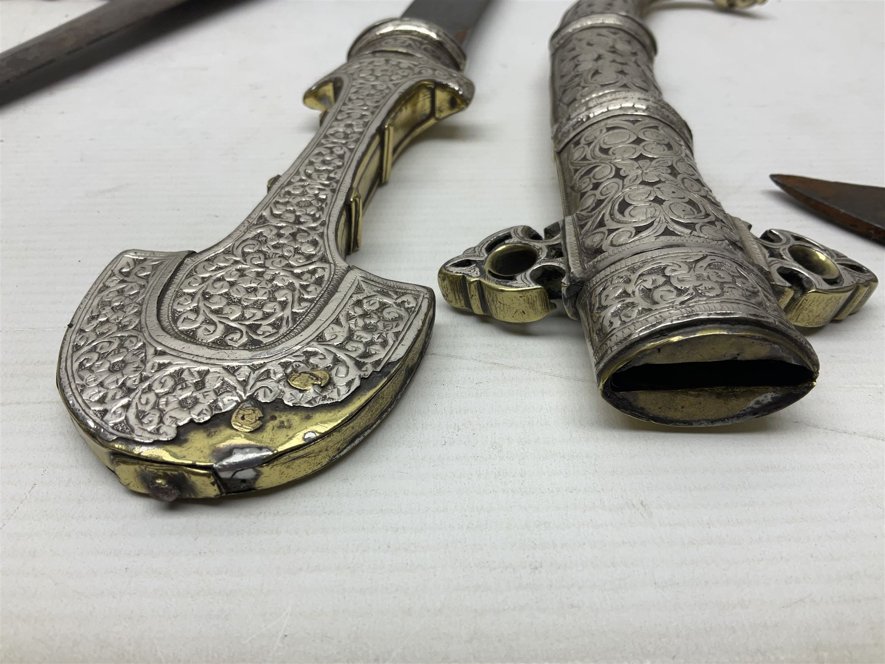 Moroccan jambiya dagger with 24.5cm plain curved blade stamped LONDON to the ricasso area, the hilt and scabbard overlaid with plain sheet brass to the back and ornate silver coloured metal to the front; waisted grip and arched pommel; two pyramid mounts to the scabbard L41cm overall; large billhook with curving blade and stacked leather washer grip; and a reproduction halberd blade (3)