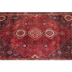 Large Persian Shiraz crimson ground carpet, the busy field decorated with a geometric pole medallion surrounded by stylised plant motifs with contrasting indigo spandrels and geometric-woven guard bands
