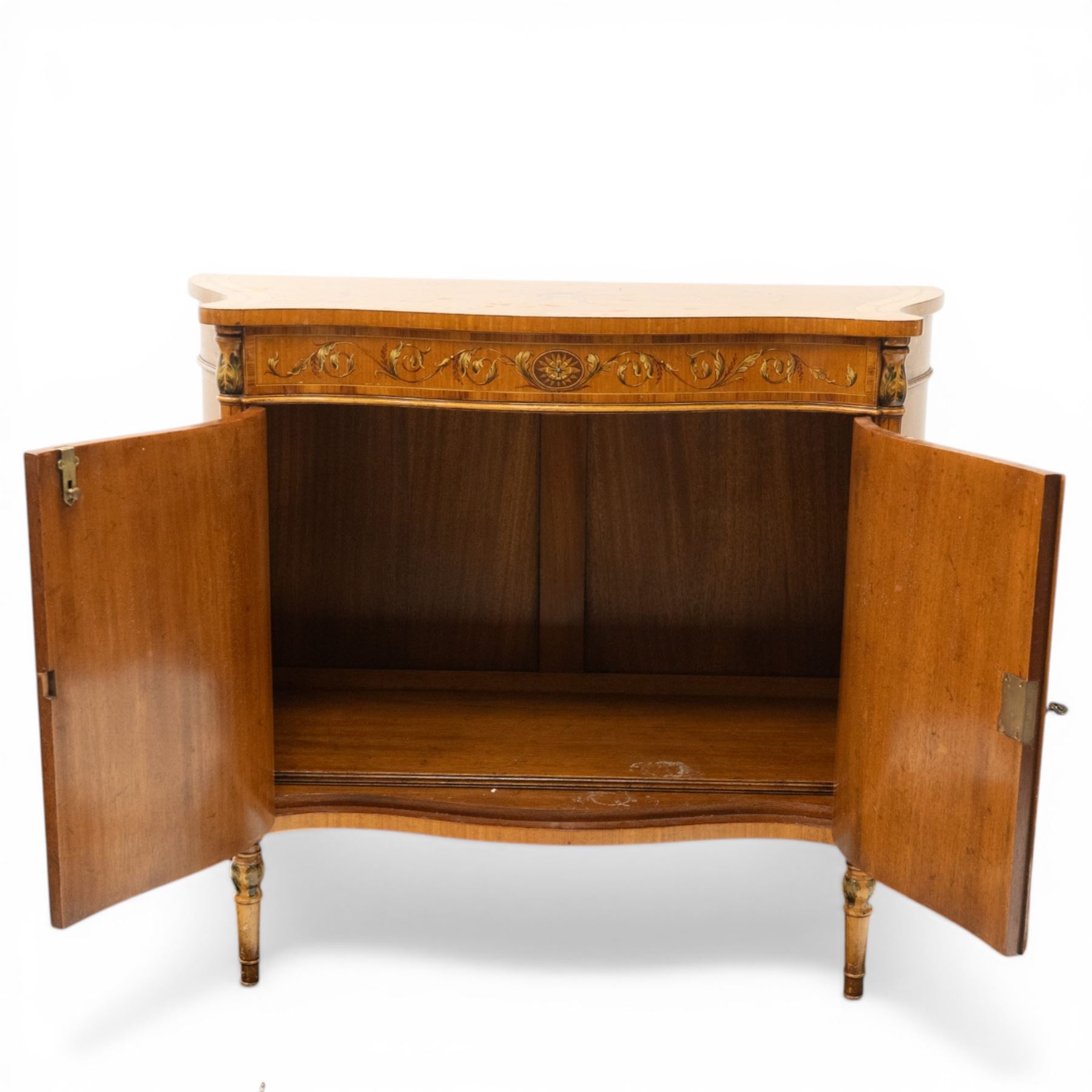 Sheraton Revival satinwood serpentine-front cabinet, the shaped cross-banded top with ebony stringing and painted scrolls of acanthi and ribbon work with a bell-flower border, the banded frieze painted with repeating acanthus scrolls, the matched veneer doors painted with oval panels of floral bouquets, raised on turned and tapering supports