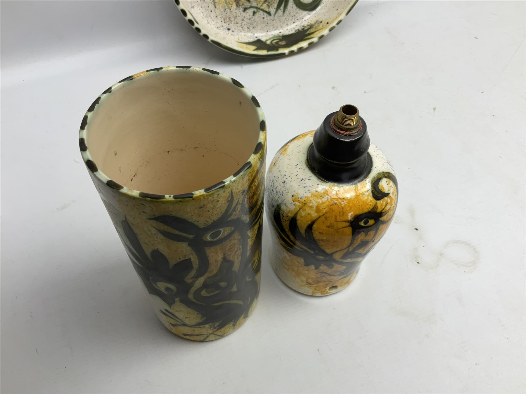 20th century Celtic Pottery, Newlyn, table lamp of tapering form, cylindrical vase and shallow bowl, all decorated with a dark stylised phoenix, modelled with wings outstretched upon sponged ochre, blue and cream ground, bowl D26cm