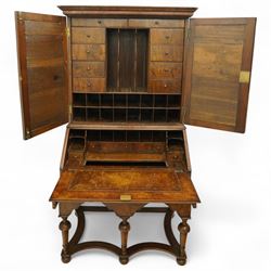 Queen Anne burr walnut chest on stand, moulded projecting cornice over arched mirror glazed doors, above a sloping fall front enclosing fitted interior with pigeonholes and correspondence drawers, fitted with foliate brass escutcheons, shaped apron over tapered baluster turned supports united by curved stretchers, early 18th century with later restorations 