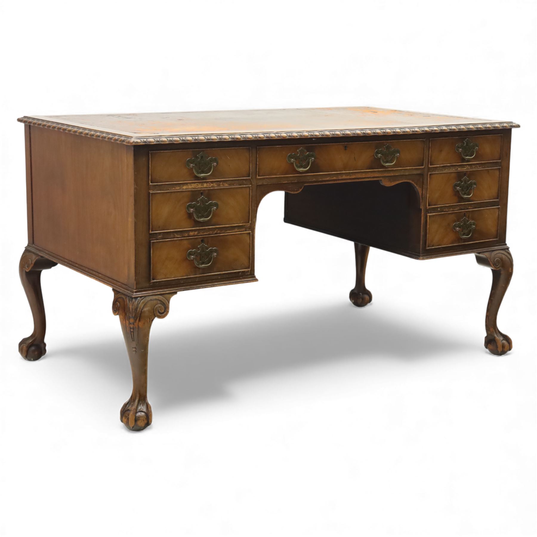 Waring & Gillow - Early 20th century mahogany desk, the leather-inset top above a shaped kneehole, central compartmented frieze drawer flanked by twin banks of of three drawers, each with brass handles, raised on cabriole legs with carved ball and claw feet (Height from floor to underside 62cm)