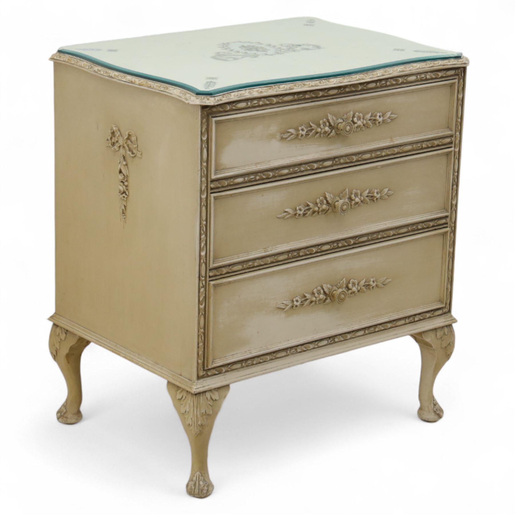 French design cream painted three drawer commode, shaped front with floral garland appliqués, fluted uprights and acanthus carved cabriole legs terminating in scroll feet