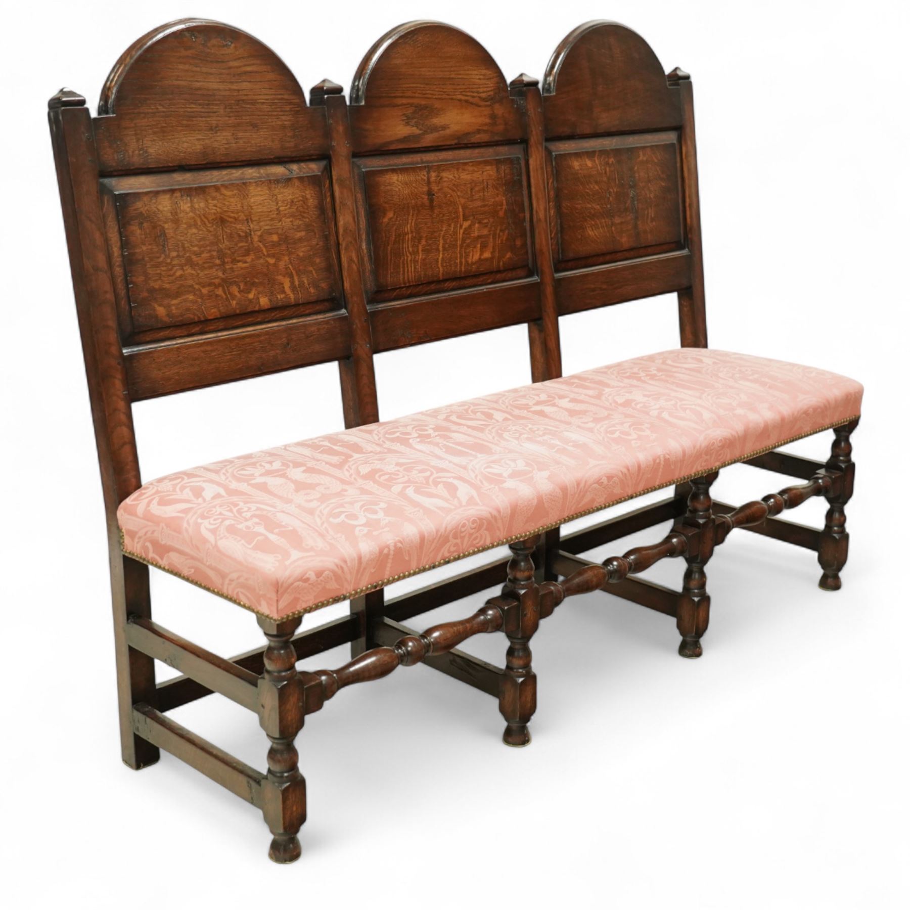 Bylaw of Ross On Wye - 17th-century design oak three-seat hall bench, triple arched panelled back, padded seat upholstered in pink damask fabric, raised on turned baluster legs united and turned front stretcher
