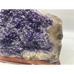 large amethyst crystal geode cluster, with well-defined crystals of various sizes, upon a carved wooden stand 