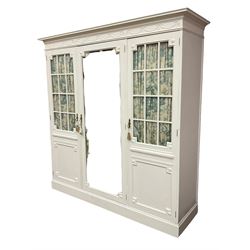 Maple and Co - Edwardian Hepplewhite design white painted triple wardrobe, foliate carved projecting cornice over ribbon and husk swag decorated frieze, two curtain lined astragal glazed doors and centre full mirror door, fitted mahogany interior including slides and drawers, plinth base, label to top of central door