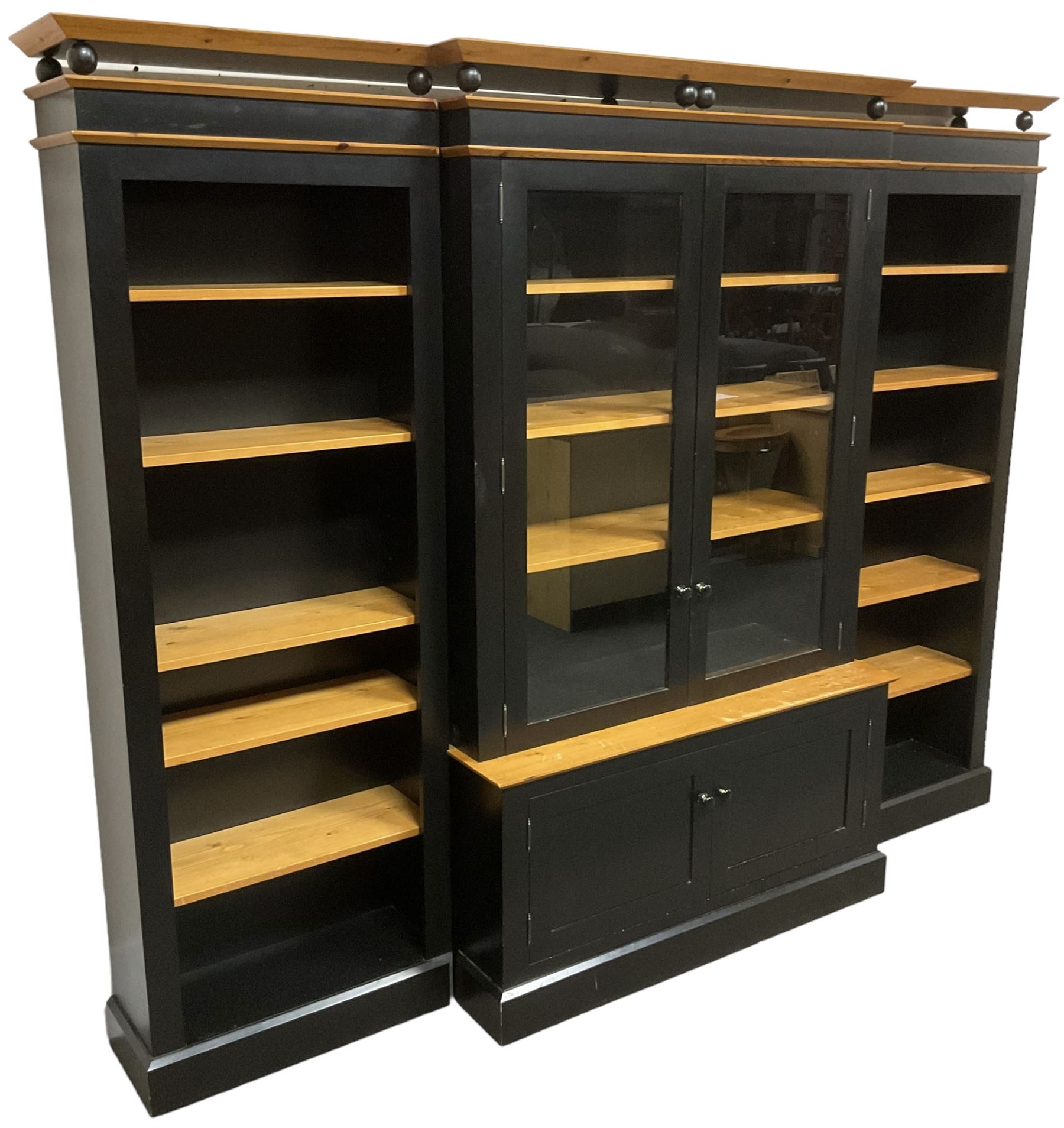 Contemporary polished pine and black finish break-front bookcase, projecting cornice over globular mounts, central cabinet enclosed by two glazed doors over double panelled cupboard, flanked by adjustable shelves, on plinth base