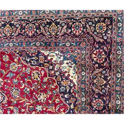 Pair of Persian wool rugs, each with rich red ground, one centred with a diamond-shaped medallion and navy spandrels within a floral field, the other with radiating floral medallion and scrolling foliate motifs, both enclosed by multiple borders with palmette and flowerhead designs, from the region of Kashan 291x376, 299 x 378 