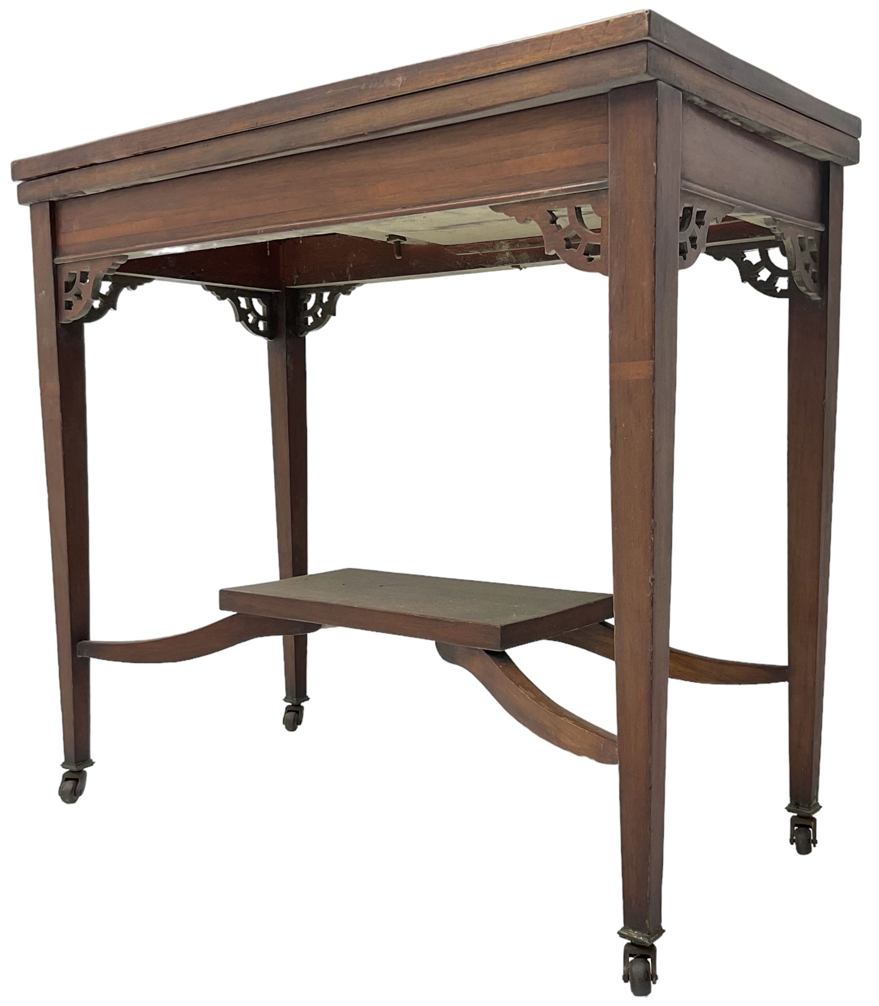 Edwardian inlaid mahogany games table, the rectangular fold-over swivel top decorated with central shell motif inlay and ebony stringing, raised on tapering supports united by shaped X-stretcher and undertier