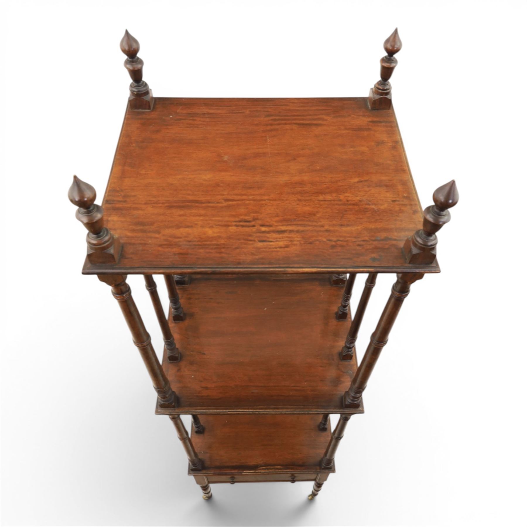 Late Victorian mahogany whatnot, the three tiers supported by turned spindle uprights with turned finials, fitted with a single frieze drawer, raised on turned supports with brass castors